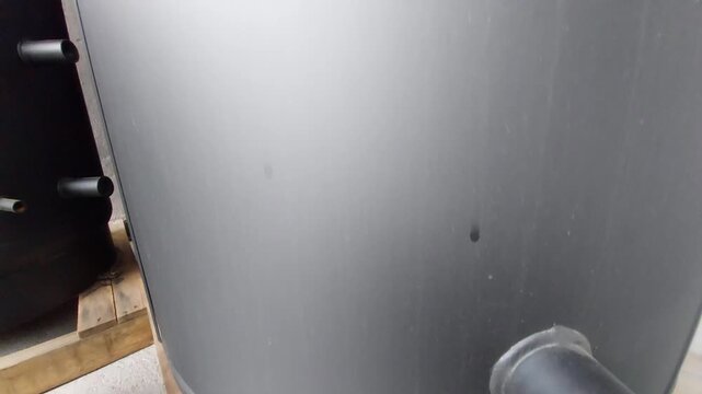Large black plastic industrial storage tank or boiler mounted on a wooden pallet floor