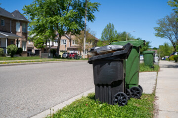 Naklejka premium Black residential garbage bin on suburban street.