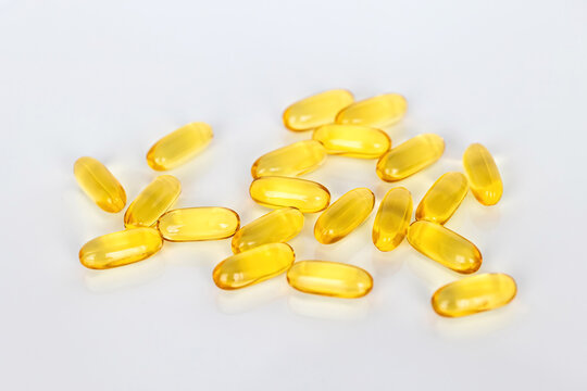 Yellow omega 3 fish oil capsules scattered on white surface with soft reflections. Healthcare, wellness and nutritional supplement concept for healthy lifestyle.