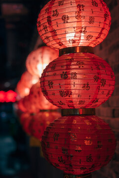 Illuminated traditional red Chinese lanterns adorn a dark brick wall during a vibrant night festival celebration
