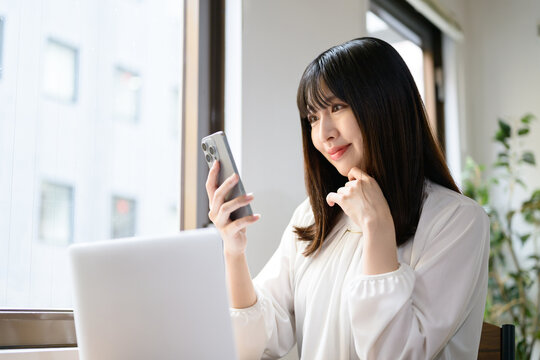 オフィスでノートパソコンとスマホを使って仕事をする日本人女性