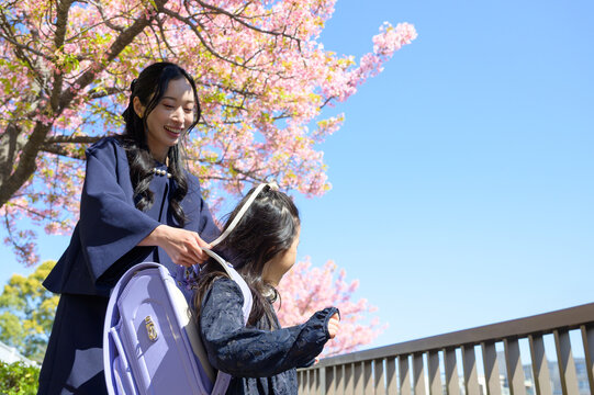 桜の下で子供にランドセルを背負わせる日本人の母親