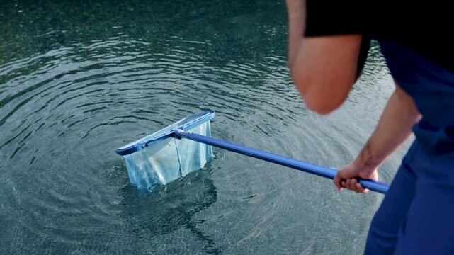 Worker performing pool maintenance, using a long-handled skimmer net to remove impurities from the clean, clear water