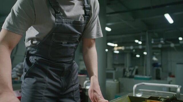 Male industrial technician in overalls using spatula knife to spread thick yellow-orange ink into ink fountain of modern offset press machine at work in printing house. Tilt up shot