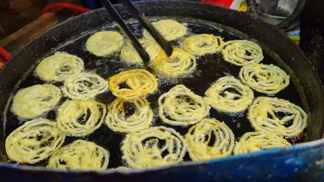 Fresh jalebi sweets frying in hot bubbling oil inside a large metal pan captured in a high quality cinematic video clip for your professional culinary projects