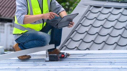 Roofer in Safety Vest Using Tablet on Metal Roof During Construction Inspection © Prathankarnpap