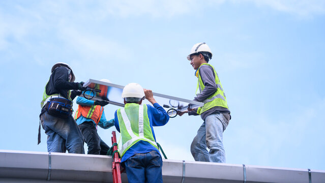 Workers Installing Solar Panel on Rooftop with Safety Gear and Hard Hats Against Blue Sky