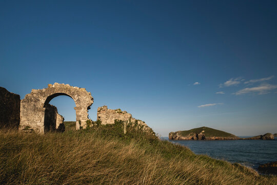 Ruins of "Ermita de San Martin"  medieval sanctuary by the sea and La Almenada island in the background. Coastline of Llanes, Asturias