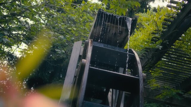 Rustic wooden water wheel turning under a gentle stream in a garden