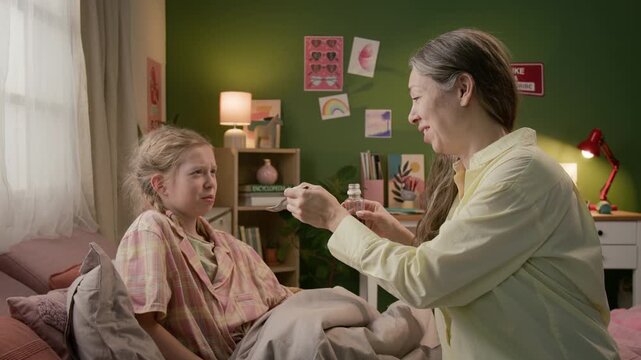 Woman pouring cough syrup onto tablespoon and giving it to sick gen alpha daughter wincing at bitterness of medicine