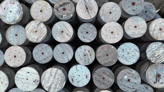 Aerial view of numerous wooden cable spools stacked closely together, showcasing their circular shapes and varied textures in a well-organized outdoor storage area