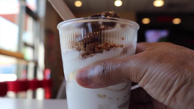 Man grabbing delicious chocolate sundae with nuts from a fast food restaurant table and leaving with the refreshing sweet dessert for a snack in summer