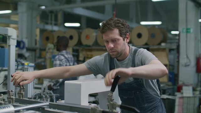Professional technician adjusting hardware clamping components of industrial printing press while operating machinery in commercial printing factory
