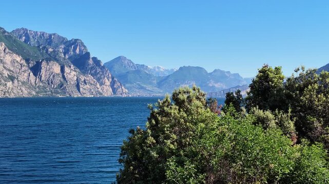Panoramic view of Lake Garda and Monte Baldo mountains with lush green Mediterranean foliage, summer travel scenery, outdoor recreation and nature exploration