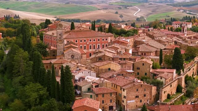 Aerial drone footage of San Quirico d'Orcia borgo with red tile roofs. Panoramic view of historic Tuscan village with rolling hills background of Val d'Orcia valley, Italy. Classical summer travel.