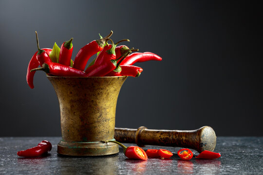Fresh red chili peppers in old brass mortar on a black table.