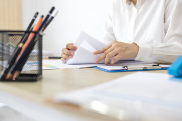 Fototapeta premium Young woman reviews documents at a bright desk. Focused, she holds a colorful highlighter. Soft natural light fills the minimalist office. Her calm expression suggests careful attention 
