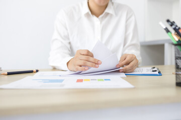 Fototapeta premium Young woman reviews documents at a bright desk. Focused, she holds a colorful highlighter. Soft natural light fills the minimalist office. Her calm expression suggests careful attention 