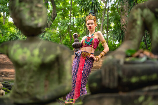 Apsara woman dressed in ancient Davaravati costume stands gracefully in the center of lush, vibrant garden carrying antique water clay jar