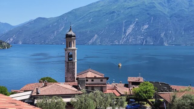 Scenic view of Limone sul Garda with church tower, alpine mountains and deep blue lake waters, travel destination and Italian summer holiday
