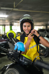 Fototapeta premium Vertical Portrait of Thai Female Delivery Courier Fastening Helmet in Garage
