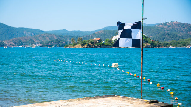 Checkered Maritime Flag on Pier with Turquoise Sea and Mountains