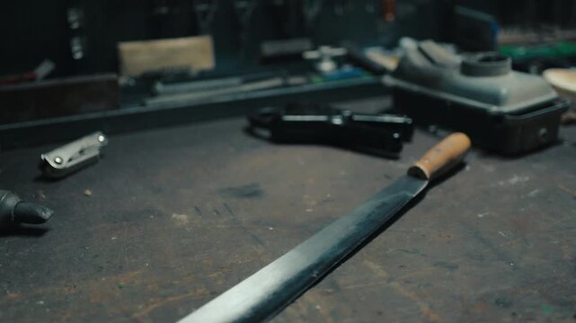 Sharp, handcrafted machete knife lying on a dirty metal table in a dark, atmospheric workshop