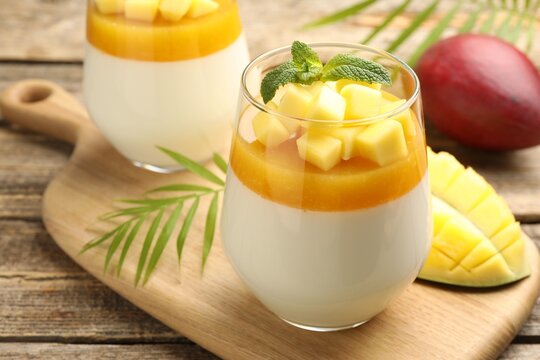 Delicious mango panna cotta with mint in glasses and fruits on wooden table, closeup
