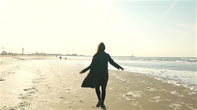 Young woman running along sandy beach beside sea waves in Dunkirk France