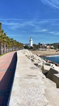 scenic view of la farola lighthouse and malagueta beach from the promenade with palm trees in malaga, spain