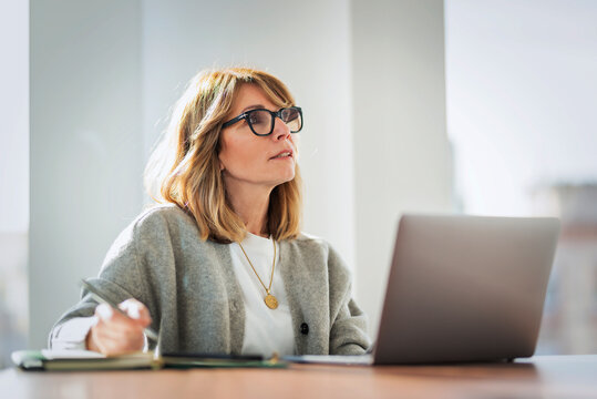 Middle-aged female professional working on a laptop in a bright modern corporate office