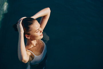 Relaxed woman floating in water, arms raised behind her head. Pool scene with sunlight and calm...