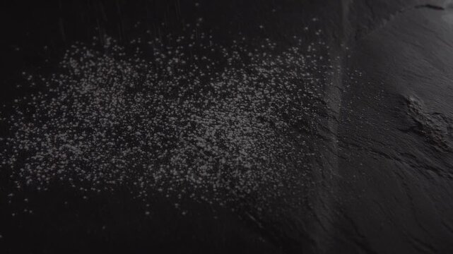 Footage of flour falling against a dark background with visible powder particles and soft lighting.