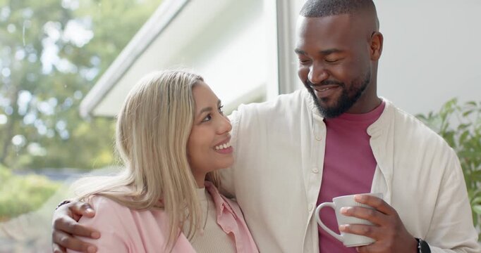Couple with African man and woman standing by window, man holding mug, glancing at mug, reflecting