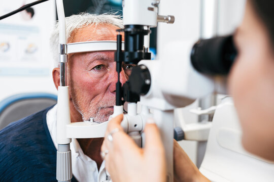 An elderly male patient undergoes a professional eye exam using a slit lamp microscope conducted by a female ophthalmologist in a modern clinic.