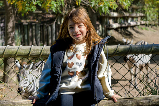Young girl smiles beside a zebra enclosure