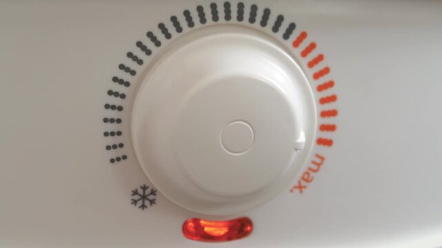 Regulator for heating cold water in boiler. Man turns temperature control on heater of water. Red light indicator comes off, boiler has turned off. Boiler heats water from cold water supply system
