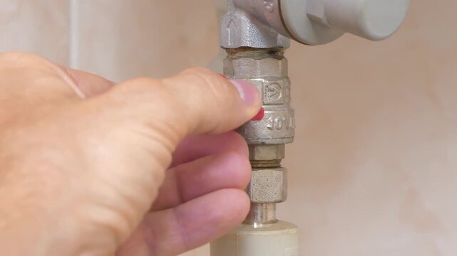 Red valve on the cold water pipe to the boiler for heating. Man turns red valve and opens the cold water supply to boiler
