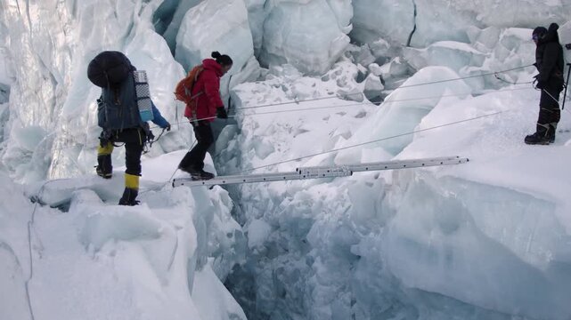 Alpinists with backpacks navigating a dangerous ice crevasse using a ladder bridge in the Himalayas