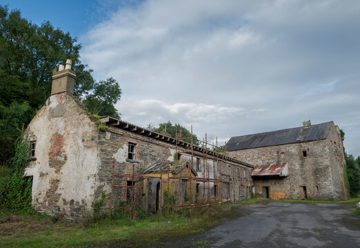 Ruins of an abandoned, industrial building shows crumbling stone and brick, with boarded-up windows and ivy climbing. Photo taken in Inniskeen, County Monaghan, Ireland