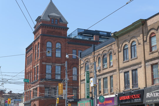 commercial block with shop signs and historic Dingman Hall, now Broadview Hotel, designed by Robert Ogilvie in Richardsonian Romanesque style, 1891-1892, located at 704 Queen E and 106 Broadview Av