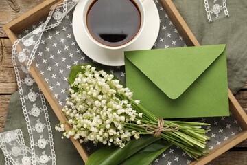 Naklejka premium Tray with beautiful lily-of-the-valley flowers, envelope and coffee on wooden table, top view