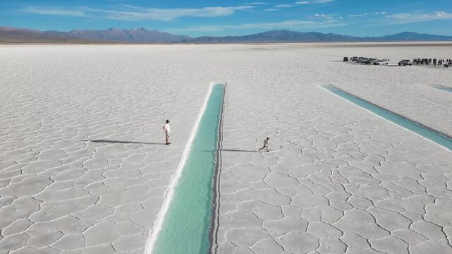 Father and child playing soccer beside turquoise saltwater pools on the salt flats of Salinas Grandes, Jujuy, Argentina