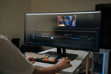 Videographer monitoring widescreen display, adjusting video timeline and audio tracks in post-production studio, crafting seamless visual narrative for digital media, close-up, cropped shot. © dikushin