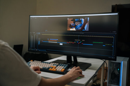 Videographer monitoring widescreen display, adjusting video timeline and audio tracks in post-production studio, crafting seamless visual narrative for digital media, close-up, cropped shot.