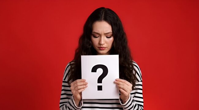 Young woman holds sign with question mark against red background, representing confusion, uncertainty, curiosity, inquiry, doubt, mystery, problem, and seeking answer