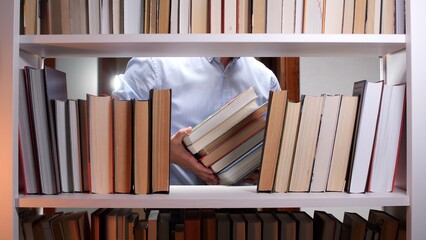 Person removing or returning a stack of books from a bookshelf, representing concepts of learning, education, knowledge, and organizing resources in a library or study space © Aliaksandr