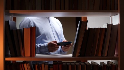 Man standing among bookshelves using a mobile phone, representing the fusion of traditional knowledge with modern digital information access and learning technology © Aliaksandr
