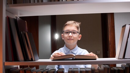 Young boy with glasses stands before a bookshelf, deeply focused on reading a book  engaged in learning, literacy and academic curiosity as he explores knowledge and growth © Aliaksandr