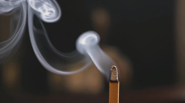 Primer plano de incienso encendido con elegantes volutas de humo blanco sobre fondo oscuro